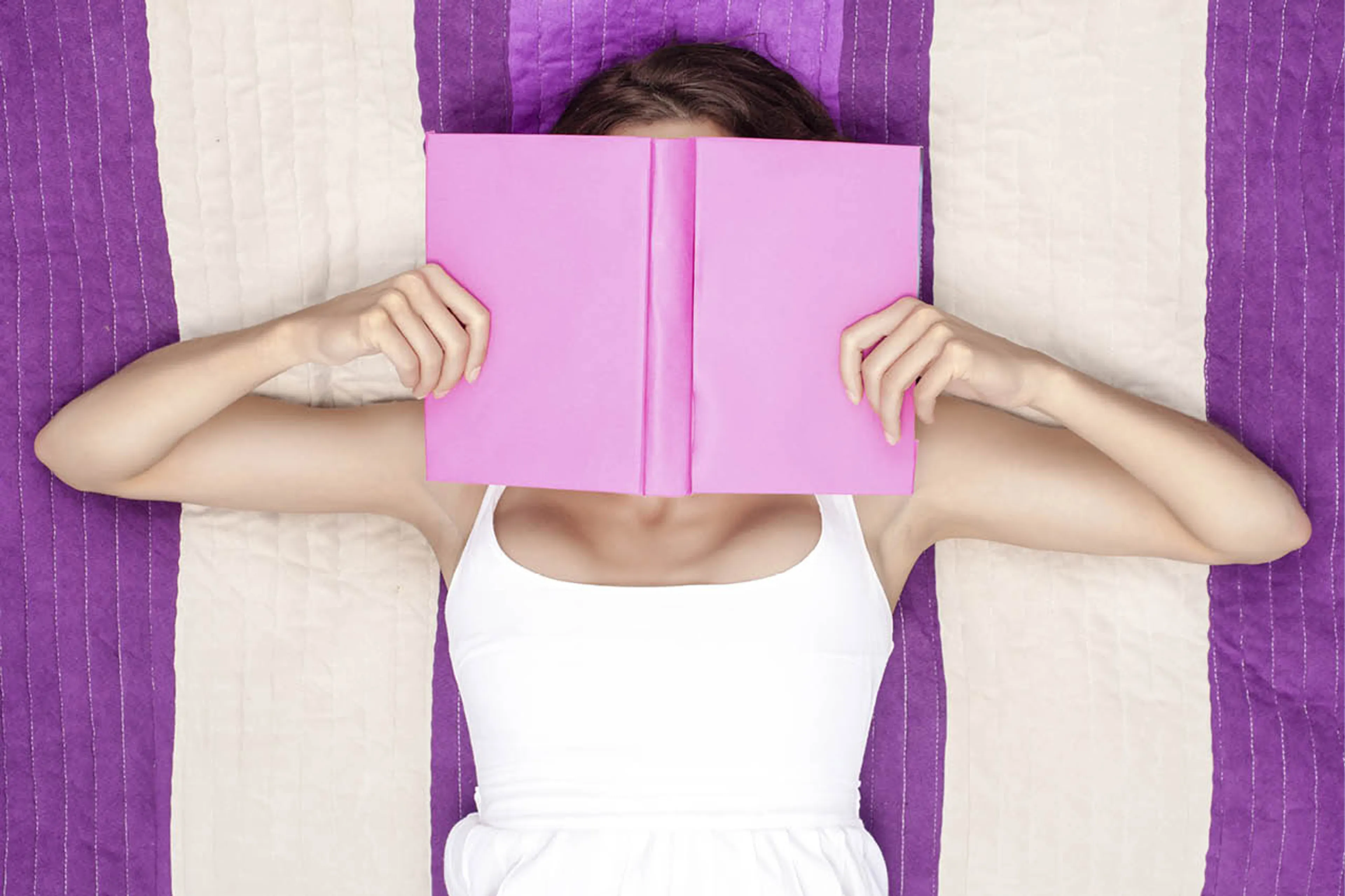 Vrouw op een paars gestreepte handdoek met een boek voor haar gezicht